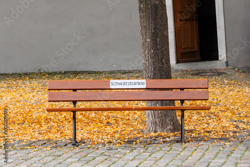 A bench in yellow autumn leaves with a text in German, Swabian dialect Schwätzbänkle which means a bench to rest and talk to each other