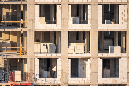 Construction site of an unfinished multi-story building. Exposed concrete and brick walls. Scaffolding visible in sunlight. Concept of urban development and construction progress