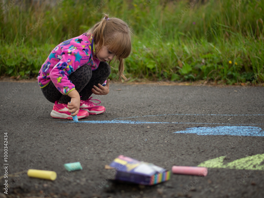 Fototapeta premium girl draws with colored chalk on the asphalt