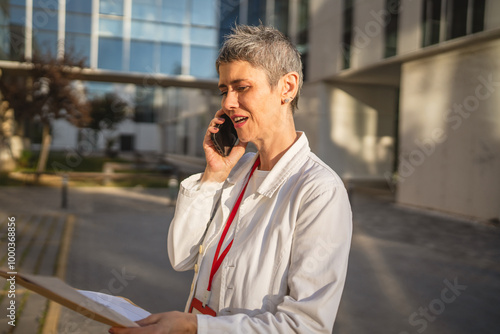 Mature woman doctor talk on cellphone read information from documents