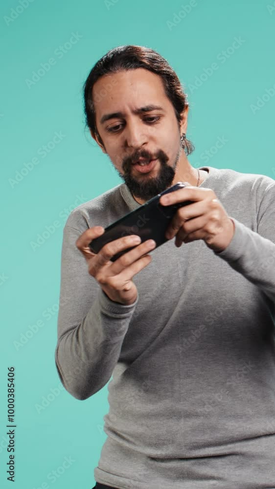 Vertical video Delighted man playing videogames on smartphone, celebrating after being victorious against opponents online, studio backdrop. Player thrilled about winning game on mobile phone, camera Vertical video Delighted man playing videogames on smartphone, celebrating after being victorious against opponents online, studio backdrop. Player thrilled about winning game on mobile phone, camera