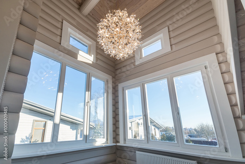 A room in a luxurious wooden house made of light logs. Chandelier with an exclusive .design. Outside the window is a sunny winter day.