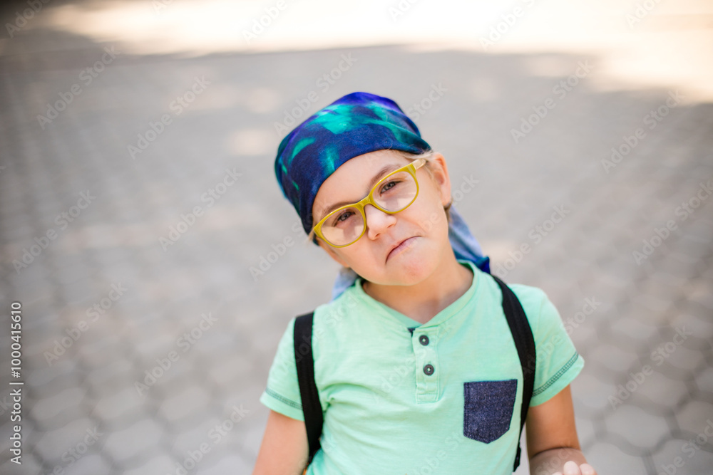 A funny little boy in glasses and a bandana, wearing a green t-shirt and denim shorts, having fun and joking A funny little boy in glasses and a bandana, wearing a green t-shirt and denim shorts, having fun and joking