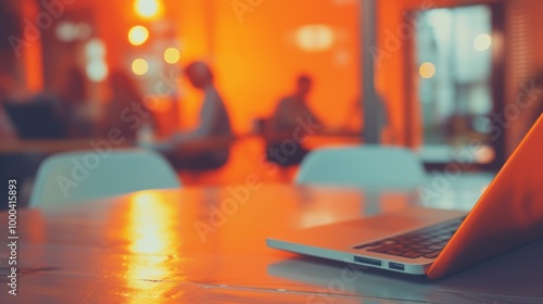 Wallpaper Mural A close-up of a laptop placed on a desk in a modern coworking space. The warm lighting and blurred background create a vibrant, collaborative atmosphere with distant figures engaged in discussion. Torontodigital.ca