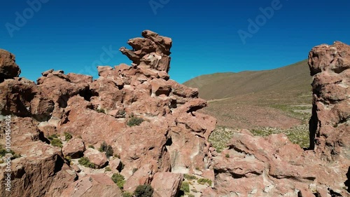 Drone flying up and revealing a large valley behind a volcanic rock formation in the Potosi distric of Bolivia. On the right the famous Camel Rock is recognizable in the distance