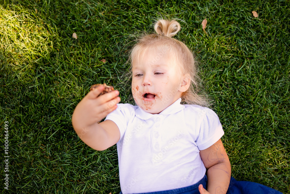 little blonde girl in school uniform sitting or lying on the grass eating delicious sweet cookies little blonde girl in school uniform sitting or lying on the grass eating delicious sweet cookies