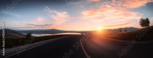 Road leading to horizon with sunset, mountains, lake, and scenic sky in the background.