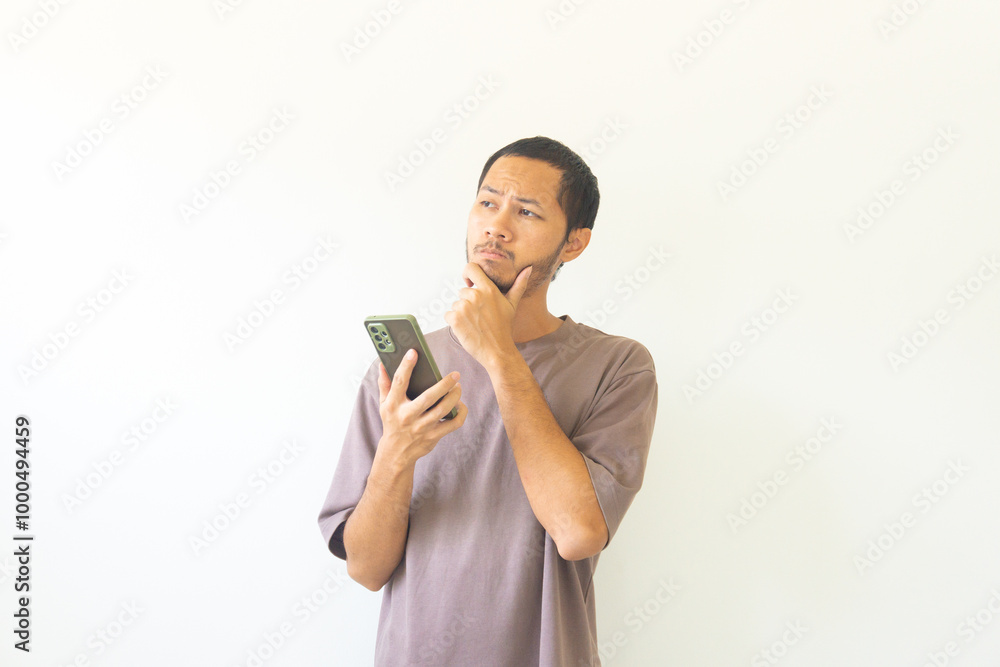 Pensive young asian men is thinking while holding smathphone on isolated white background Pensive young asian men is thinking while holding smathphone on isolated white background