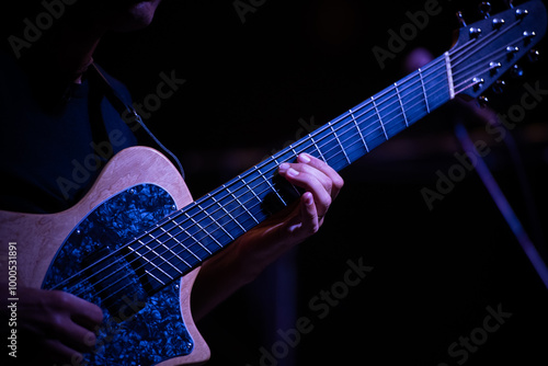 Photography Close-up of a guitarist's hand strumming the strings of an electric guitar during a live jazz performance, with dramatic lighting