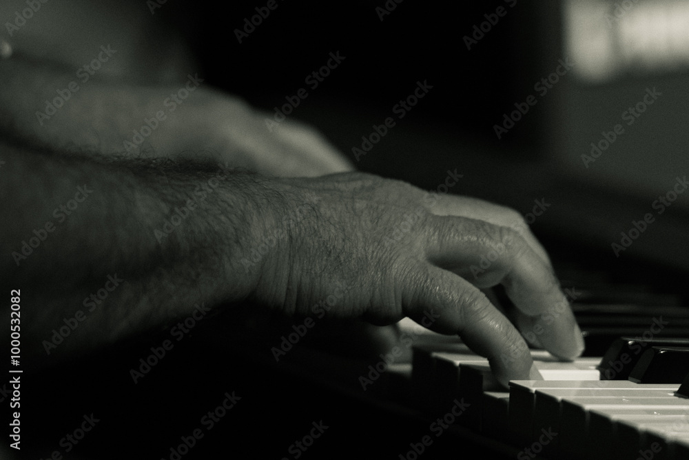 Fototapeta premium Black and white photo of a musician's hand playing a piano. The close-up captures the texture and movement, highlighting the artistry of the pianist in a jazz setting.