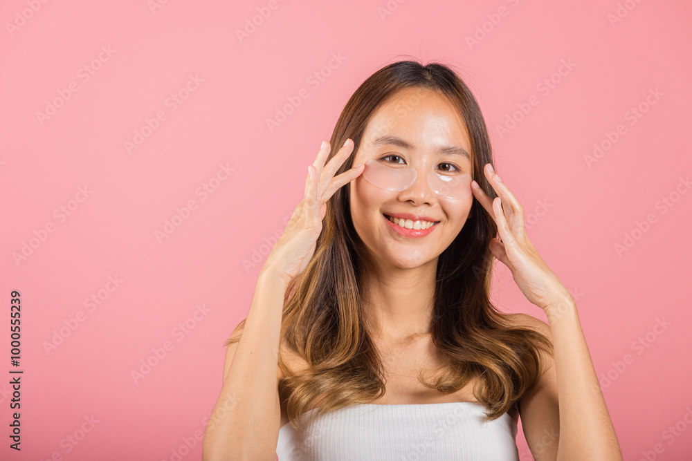 Anti aging. Asian beautiful young woman smiling mask cosmetic patches gel under the eyes, Portrait female applying medical hydrogel eye patch on face, studio shot isolated on pink background, skincare Anti aging. Asian beautiful young woman smiling mask cosmetic patches gel under the eyes, Portrait female applying medical hydrogel eye patch on face, studio shot isolated on pink background, skincare
