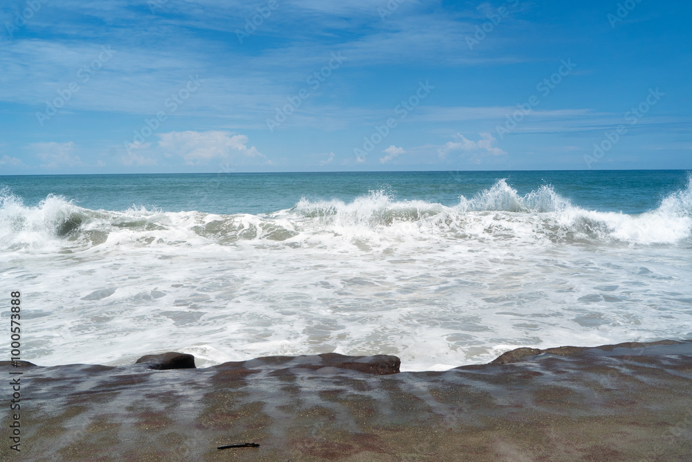 a blue rough ocean surf crashes over and over and forms a white sea foam as it trickles onto the flat slab of rock on the beach a blue rough ocean surf crashes over and over and forms a white sea foam as it trickles onto the flat slab of rock on the beach
