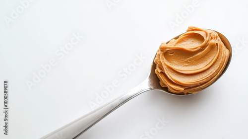 A spoonful of creamy peanut butter sits atop a silver spoon, against a clean white background, ready to be enjoyed.