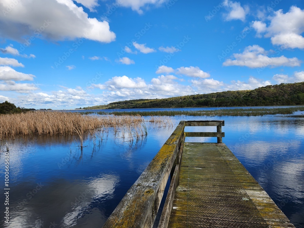 Wooden jetty on lake with reeds clouds and sky Wooden jetty on lake with reeds clouds and sky