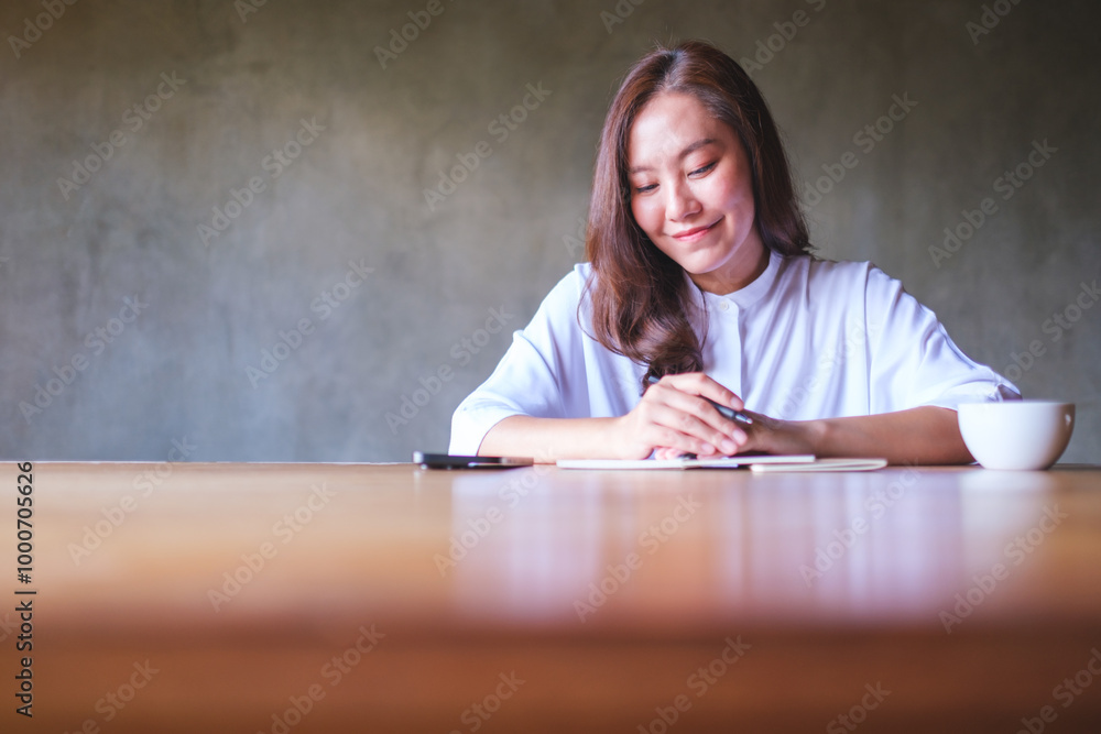 Portrait image of a woman writing on a notebook with mobile phone and coffee cup on wooden table Portrait image of a woman writing on a notebook with mobile phone and coffee cup on wooden table