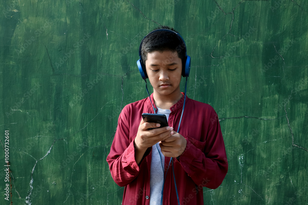 Fototapeta premium A teenager who is using their headphones and cellphone.
