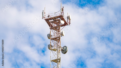A tall tower with a lot of antennas on top. The sky is blue with some clouds. The tower is a cell phone tower