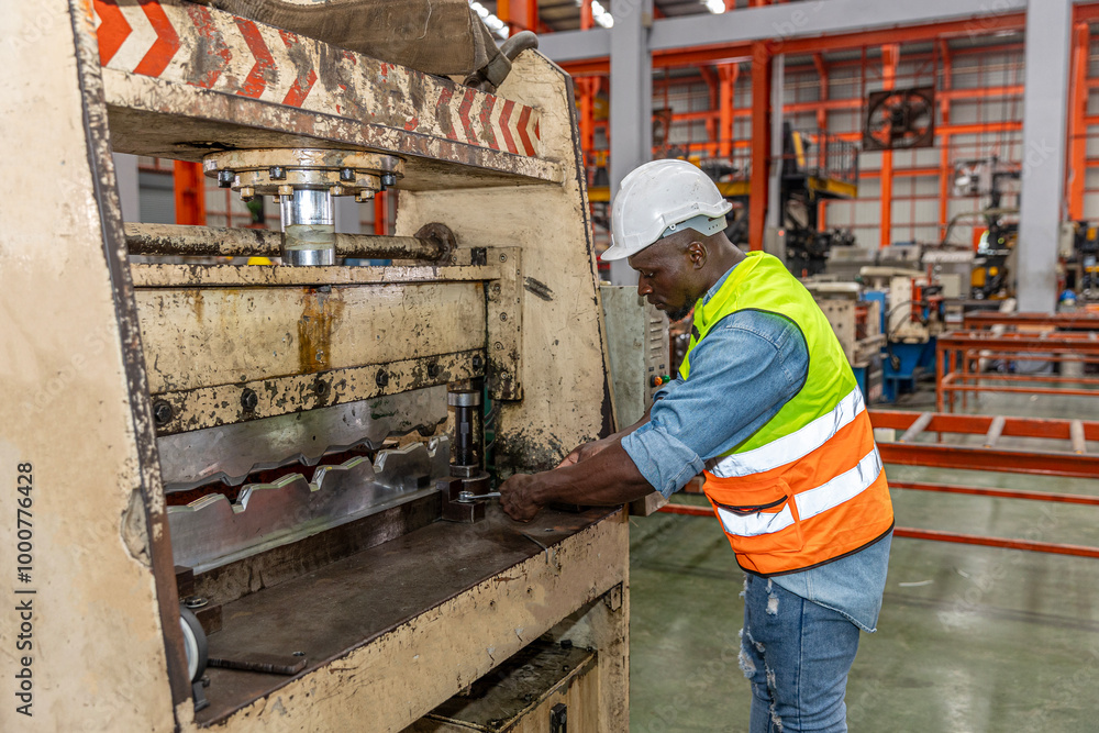An African metal engineer or technician is checking the iron roof forming machine for the next operation in a factory. Metal worker in safety dress is repairing the roof forming machine. An African metal engineer or technician is checking the iron roof forming machine for the next operation in a factory. Metal worker in safety dress is repairing the roof forming machine.