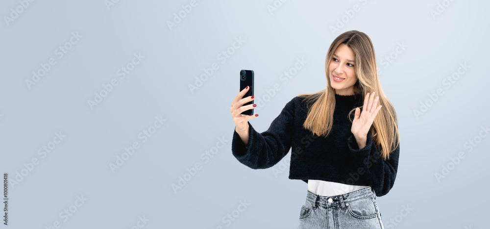 Woman taking a selfie and waving on light blue background. Woman taking a selfie and waving on light blue background.