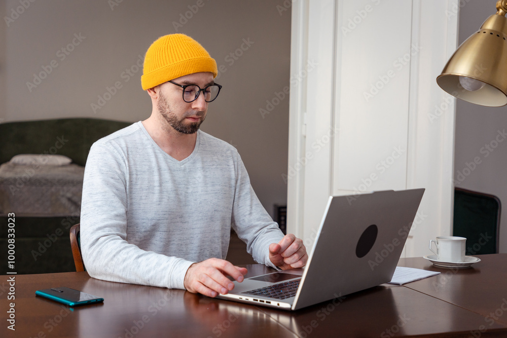 Caucasian man wearing hat and glasses is working at laptop. Remote work from the home office. The concept of freelancing Caucasian man wearing hat and glasses is working at laptop. Remote work from the home office. The concept of freelancing