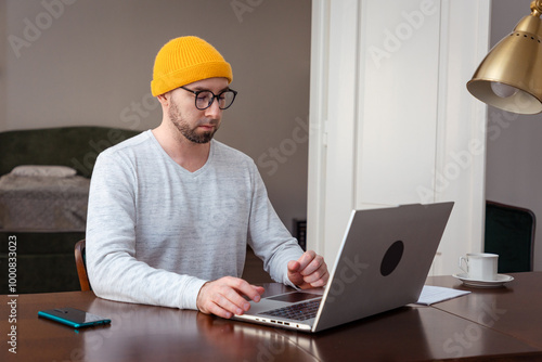 Caucasian man wearing hat and glasses is working at laptop. Remote work from the home office. The concept of freelancing