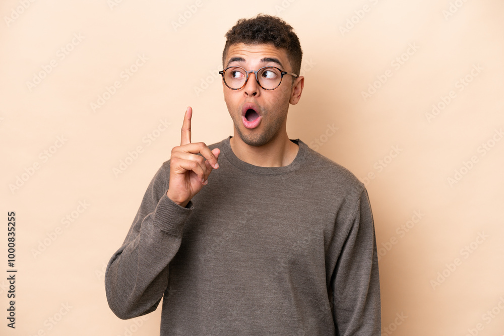 Fototapeta premium Young Brazilian man isolated on beige background thinking an idea pointing the finger up