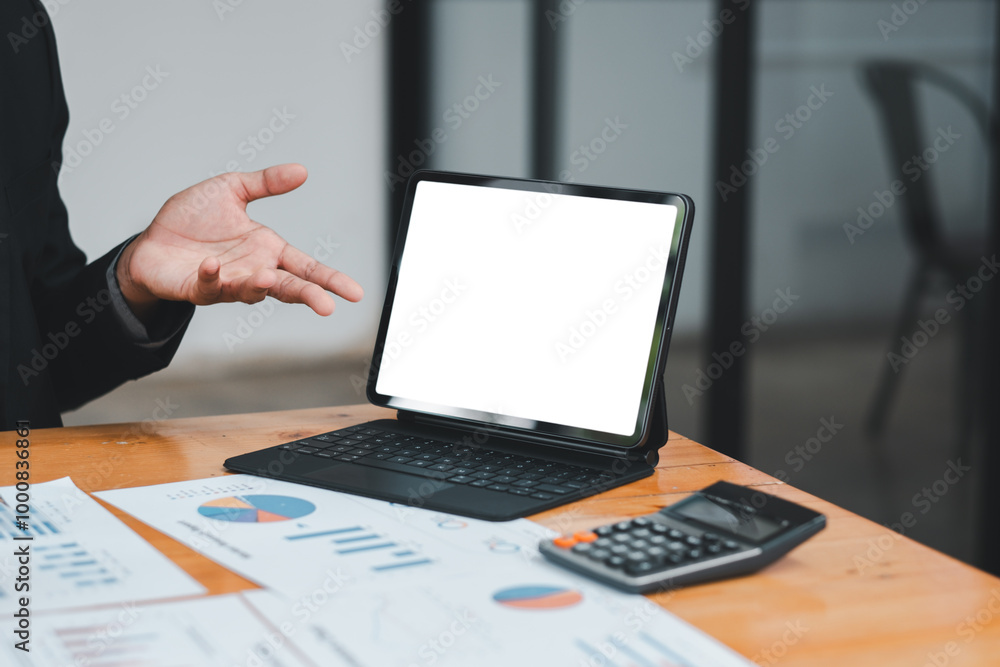 A business professional presenting data using a digital tablet with financial charts and a calculator on a wooden desk. A business professional presenting data using a digital tablet with financial charts and a calculator on a wooden desk.