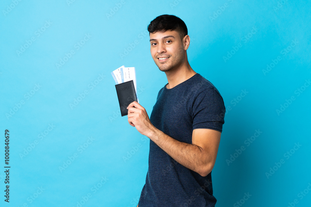 Young Colombian man isolated on blue background happy in vacation with passport and plane tickets Young Colombian man isolated on blue background happy in vacation with passport and plane tickets