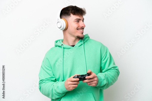 Young handsome man playing with a video game controller isolated on white background looking to the side and smiling photo