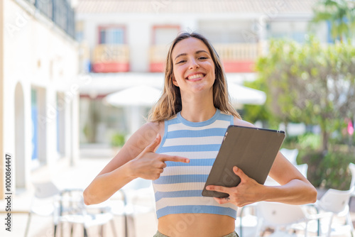 Young pretty woman holding a tablet at outdoors and pointing it Free Download Young pretty woman holding a tablet at outdoors and pointing it - GFXLoad