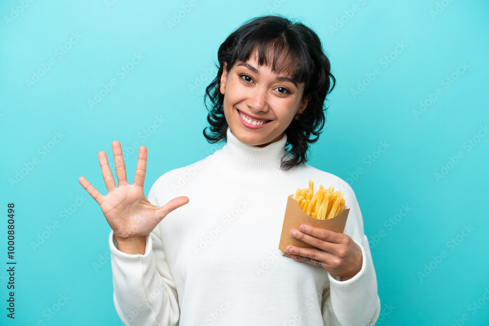 Young Argentinian woman holding fried chips isolated on blue background counting five with fingers Young Argentinian woman holding fried chips isolated on blue background counting five with fingers
