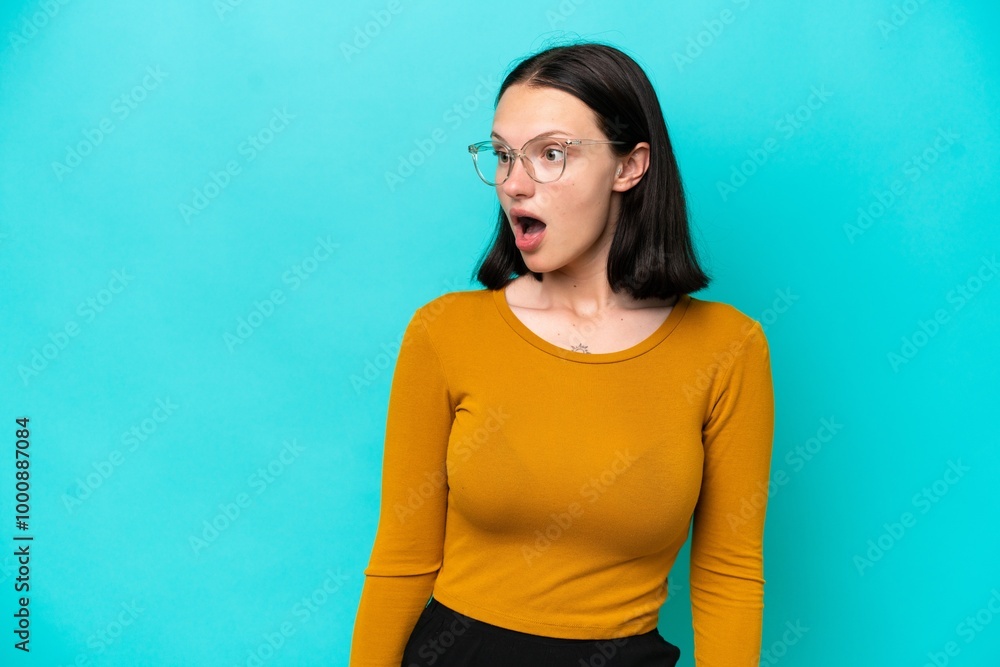 Young caucasian woman isolated on blue background doing surprise gesture while looking to the side Young caucasian woman isolated on blue background doing surprise gesture while looking to the side