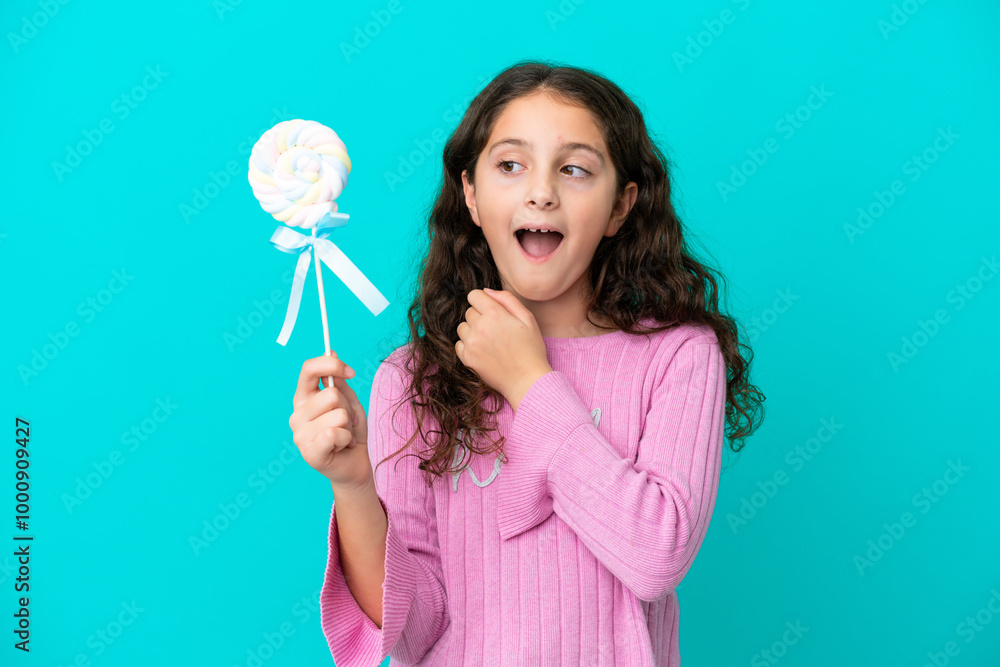 Little caucasian girl holding a lollipop isolated on blue background with surprise and shocked facial expression Little caucasian girl holding a lollipop isolated on blue background with surprise and shocked facial expression