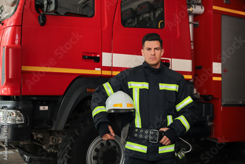 Portrait of firefighter in uniform with helmet near fire truck at station, space for text