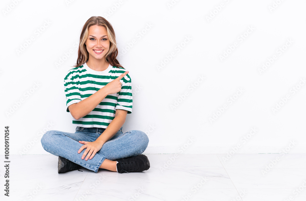 Young Russian girl sitting on the floor isolated on white background pointing to the side to present a product Young Russian girl sitting on the floor isolated on white background pointing to the side to present a product