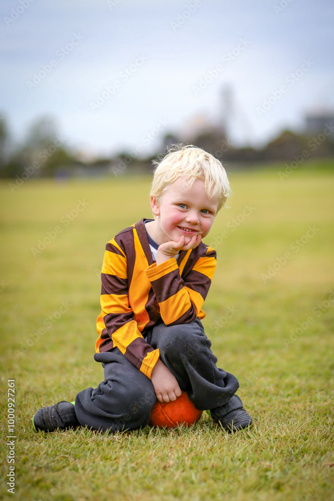 Little boy in Aussie Rules Football uniform on field with ball Little boy in Aussie Rules Football uniform on field with ball