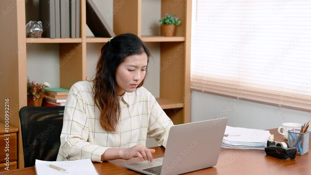 Office woman sitting working in front computer screen placed on table in front, eyes turned look at work information in document placed near computer, had confused look on face with job had received. Office woman sitting working in front computer screen placed on table in front, eyes turned look at work information in document placed near computer, had confused look on face with job had received.