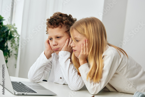 Happy siblings studying together at home using a laptop for online education The young boy and girl are sitting at a table in their living room, fully engaged in their elearning lessons With focused