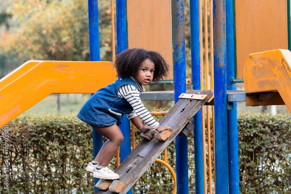 Young Afro hair elementary schoolgirl crawling through colorful tunnel on a playground, weekend carefree holiday in park. bright playground equipment and focus expression capture childhood exploration