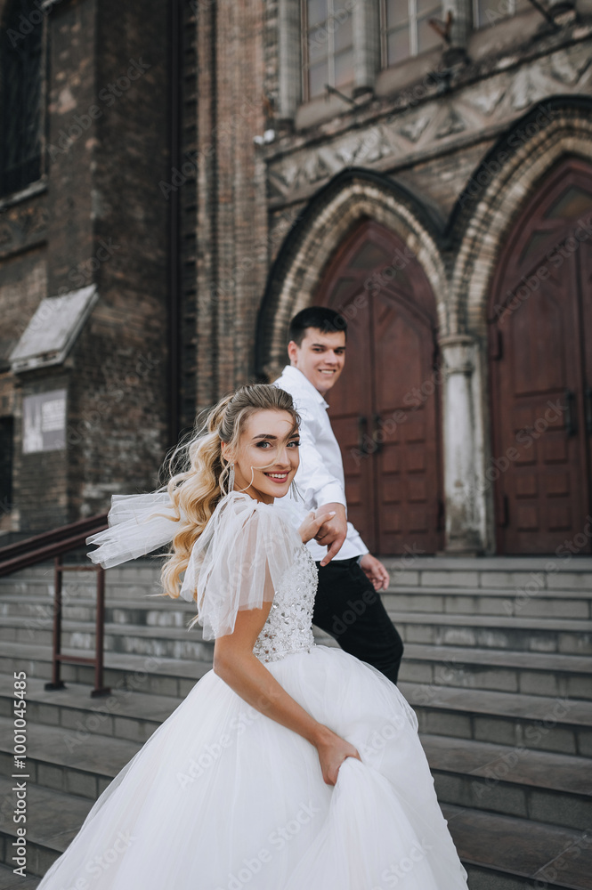 Stylish young groom and beautiful smiling bride curly blonde in white lace dress hug, walk together against the background of old brick retro church. Wedding photo, portrait of happy newlyweds. Stylish young groom and beautiful smiling bride curly blonde in white lace dress hug, walk together against the background of old brick retro church. Wedding photo, portrait of happy newlyweds.