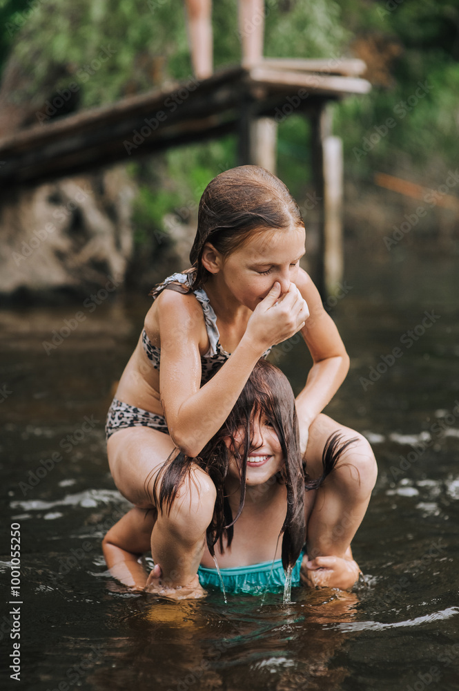 Fototapeta premium Two girlfriends girls, cheerful smiling children play, laugh, jump in the water in the lake on the sea. Photography, portrait, friendship concept, rest.