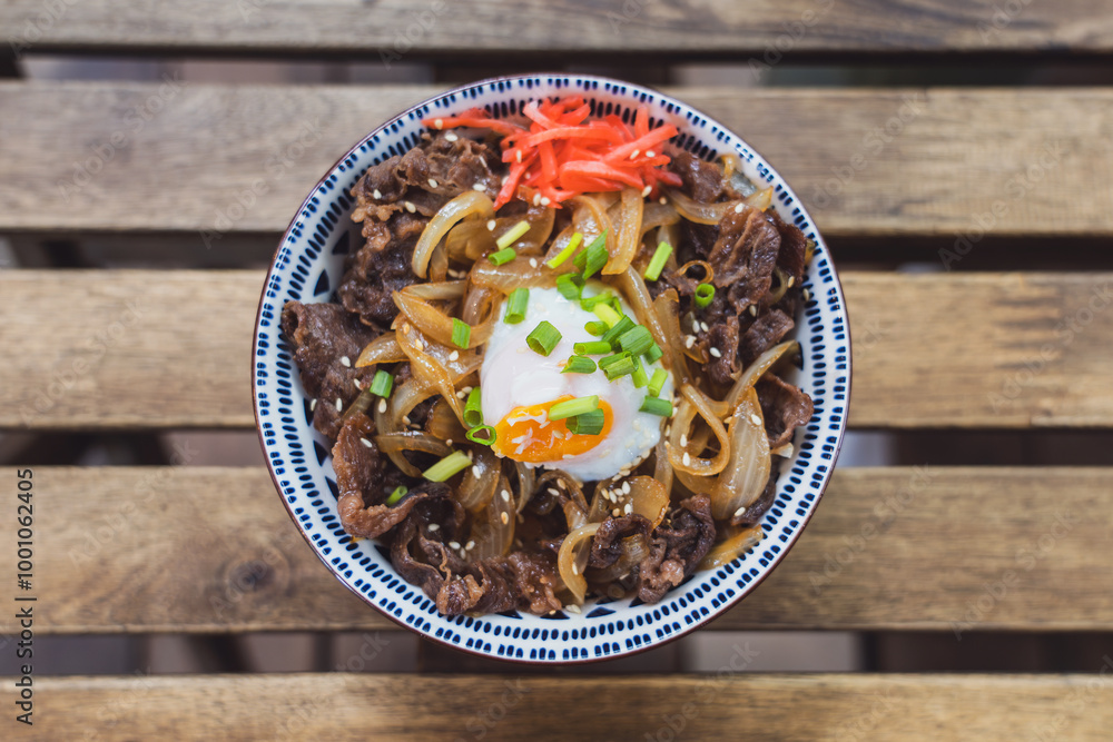 Gyudon Japanese Beef Bowl with Onsen Egg in ceramic bowl on a slatted table in a cafe restaurant. Gyudon Japanese Beef Bowl with Onsen Egg in ceramic bowl on a slatted table in a cafe restaurant.