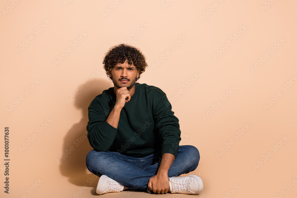 Full size photo of nice young man sit floor ponder wear sweater isolated on beige color background Full size photo of nice young man sit floor ponder wear sweater isolated on beige color background