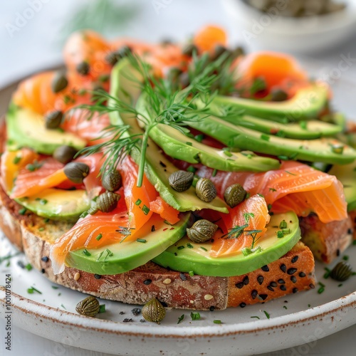 a sumptuous serving of fresh raw salmon slices, slices of avocado served on a toasted bread, loaded with capers and sprinkled with black pepper