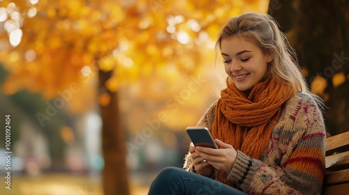 A young woman sitting on a bench, smiling at her phone with vibrant autumn trees in the background.
