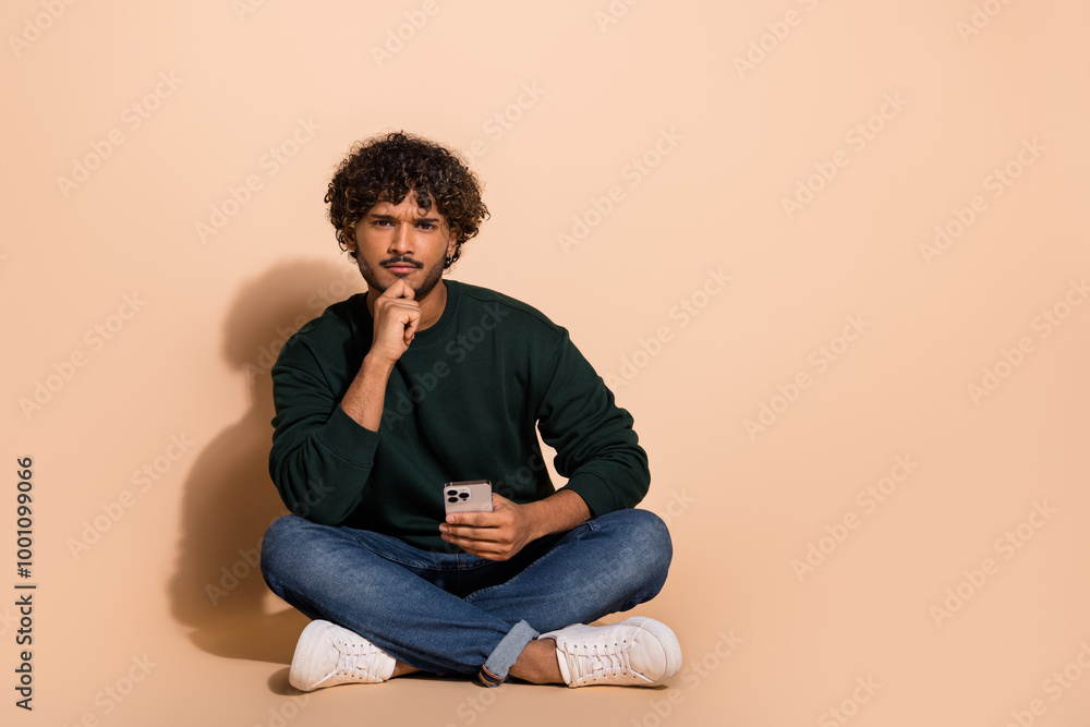 Full size photo of nice young man hold phone think wear sweater isolated on beige color background Full size photo of nice young man hold phone think wear sweater isolated on beige color background