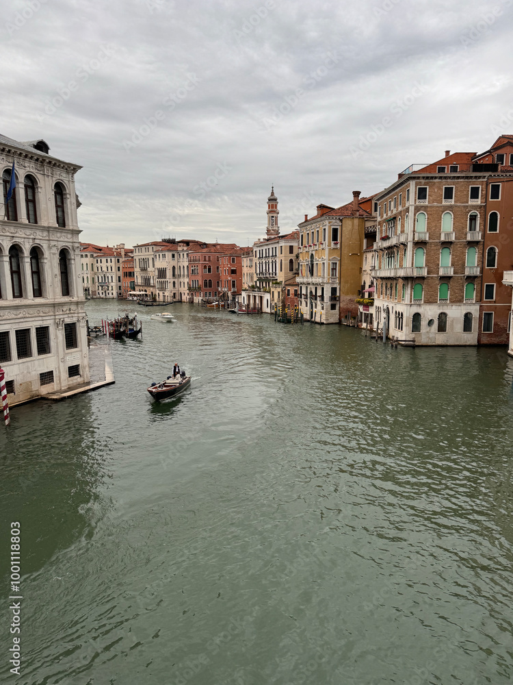 Obraz premium A view of canal in Venice with a gondola in the water and beautiful buildings lining the sides. The sky is overcast but the water is still sparkling. The scene is peaceful and serene.