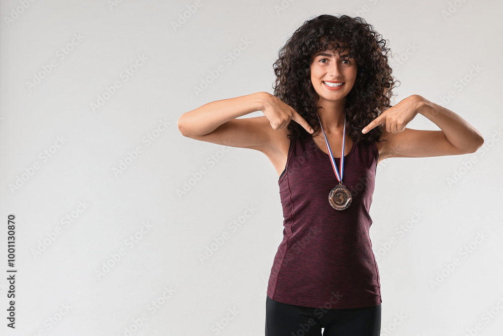 Happy winner pointing at her bronze medal on light grey background. Space for text Happy winner pointing at her bronze medal on light grey background. Space for text