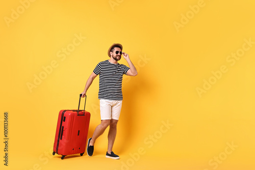 Happy man in sunglasses with suitcase walking on orange background