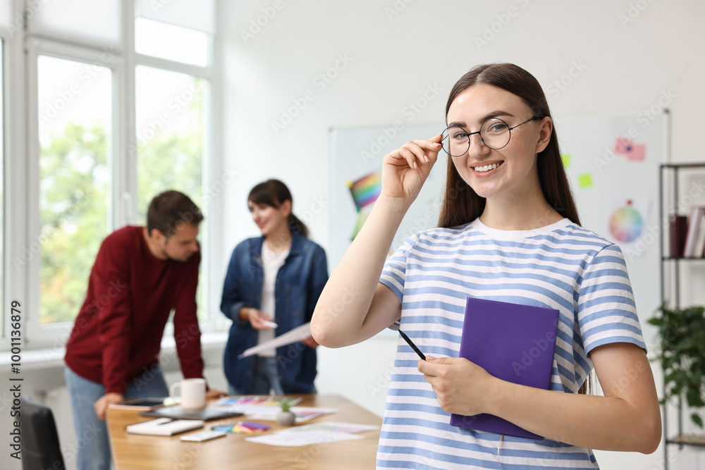 Portrait of happy young designer with notebook in office